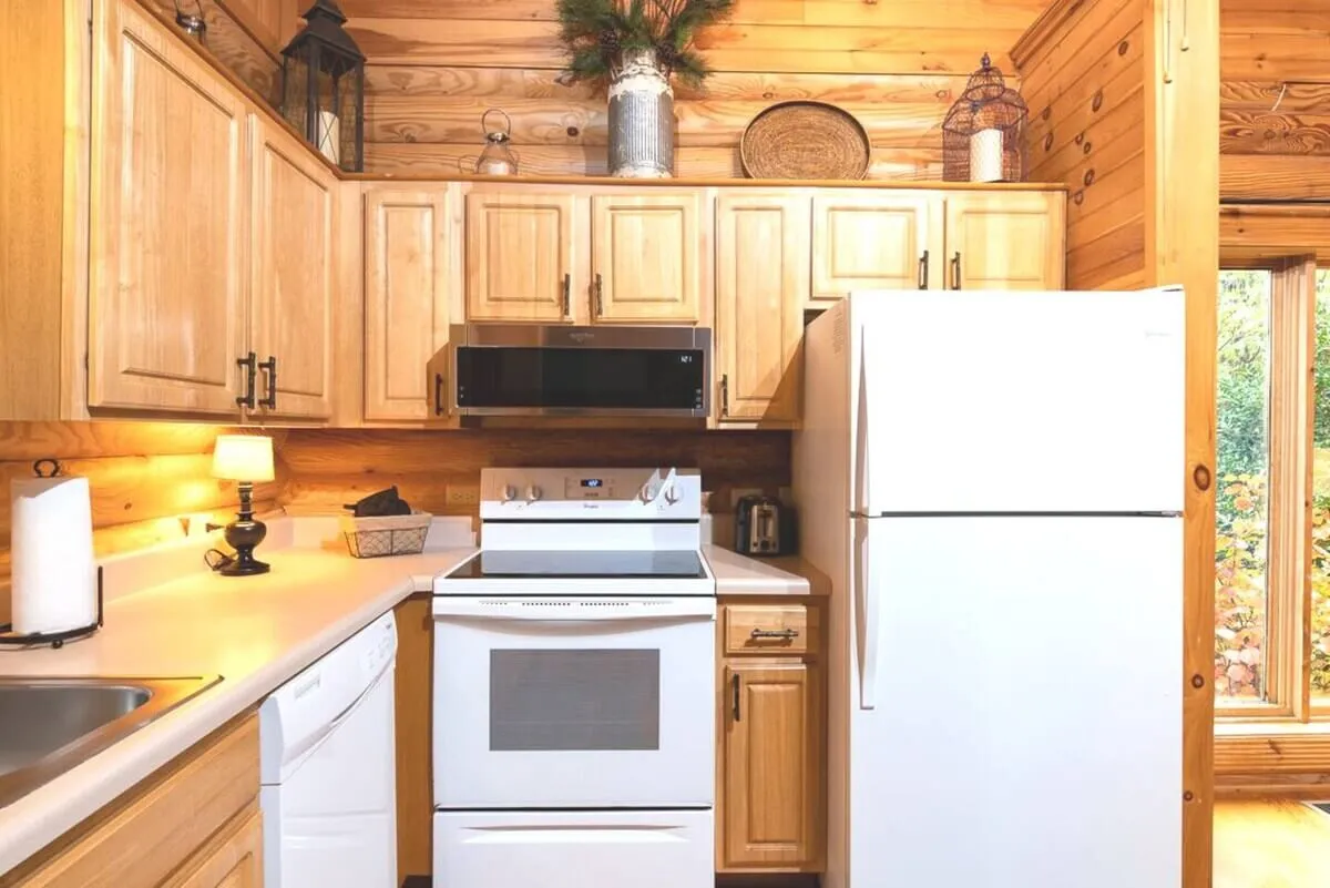 A warm, inviting kitchen features white appliances, wooden cabinets, and decorative items on open shelves. The kitchen is spacious with ample counter space, creating a comfortable area for cooking and socializing. The soft glow from the lighting gives the space a homey, welcoming atmosphere.