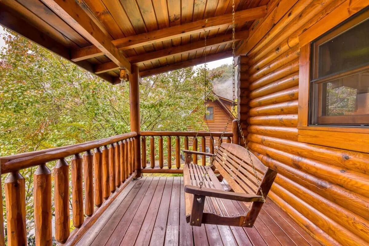 A wooden porch swing with log railings nestled among tall trees, offering a secluded space for conversation or simply enjoying the peaceful environment. The scene feels private and tranquil, ideal for intimate moments.