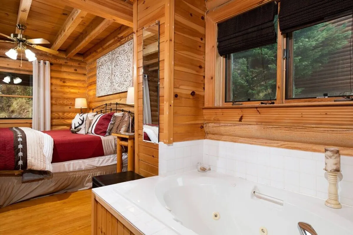 This interior scene features a cozy bedroom with wooden paneling, a bed with decorative pillows, and a whirlpool tub illuminated by natural light streaming through the windows. It exudes warmth and relaxation, suggesting comfort after a day outdoors.