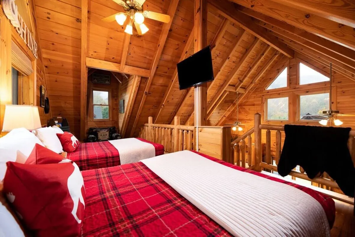 A spacious bedroom with two beds dressed in plaid blankets, a wooden ceiling, and large windows that let in natural light. The space is ideal for families or groups, offering a cheerful and comfortable setting for relaxation and bonding. The decor is simple yet inviting, with an emphasis on comfort and communal rest.