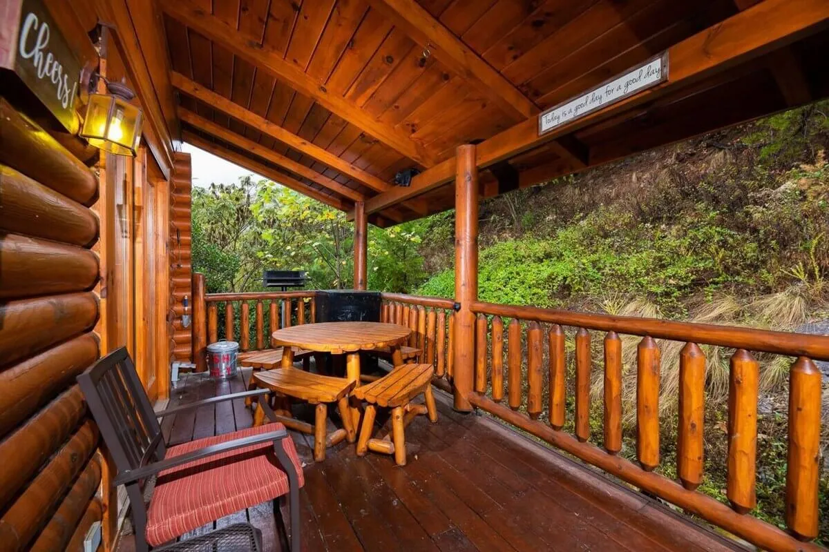A spacious wooden deck set amidst greenery, featuring a round table and chairs designed for relaxed outdoor dining or gathering. The abundant surrounding foliage reinforces the sense of privacy and seclusion.